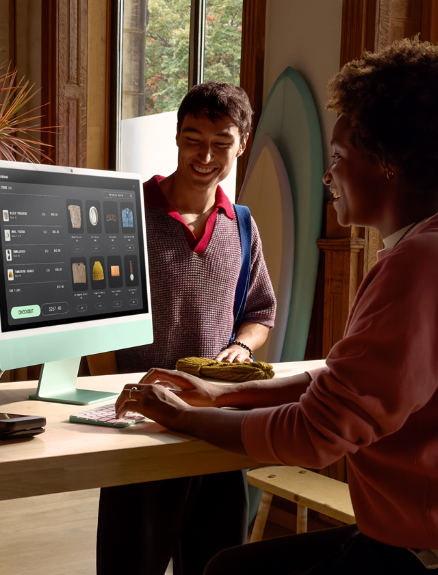 บุคคล 2 คนกำลังดูผลิตภัณฑ์บนจอภาพกระจก Nano-texture ของ iMac อยู่ในห้องที่มีแสงสว่างเพียงพอ